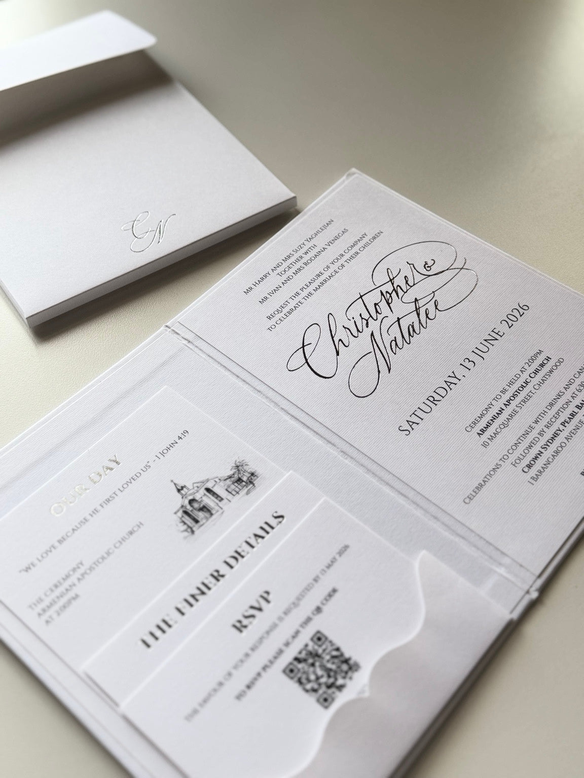 Open white invitation booklet with a pocket of details cards on the left and calligraphy invitation on the right.