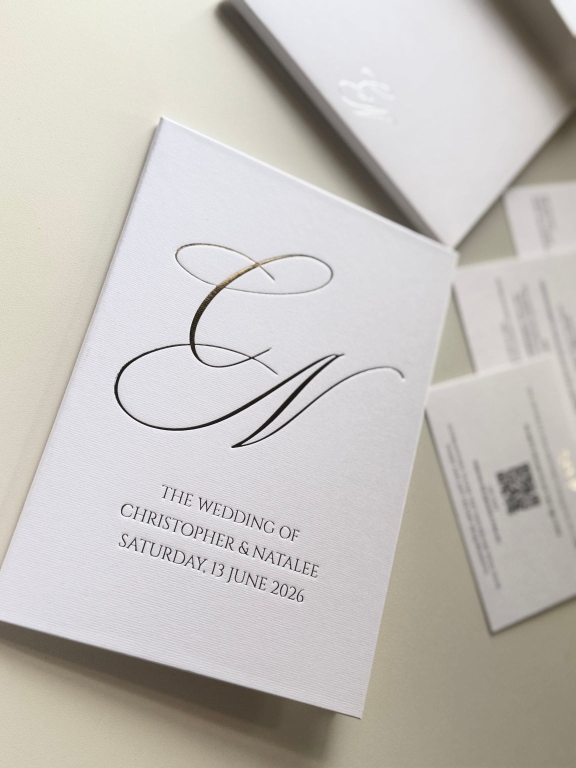 Closed white wedding invitation booklet with an oversized CN monogram and Christopher and Natalee wedding details.