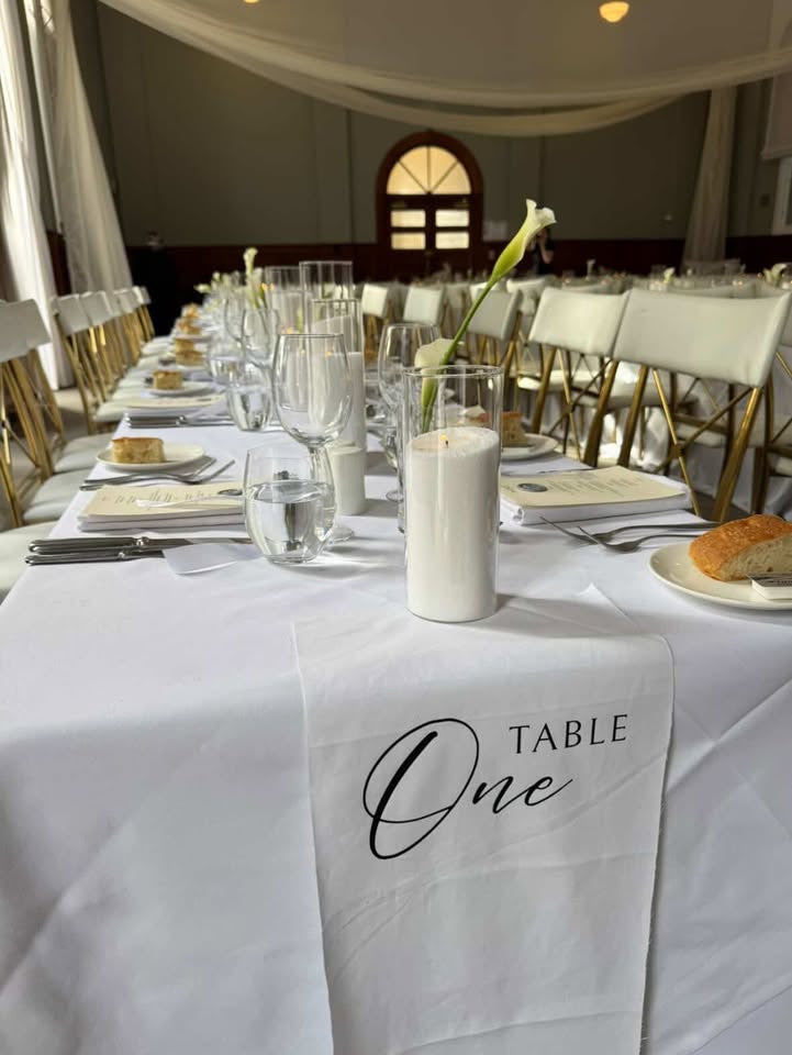 Reception table styled with white linens, candles, glassware and white flowers.